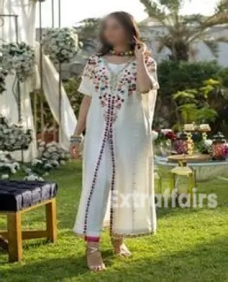 A Call girl in noida in a white, intricately embroidered dress stands on a grassy lawn. She is holding a necklace and surrounded by floral decor.