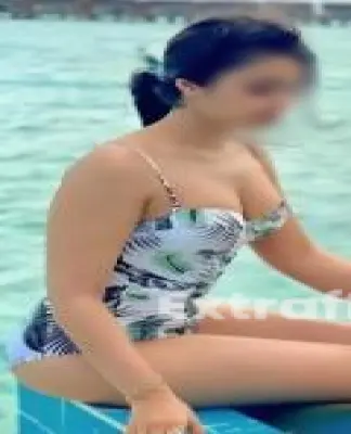 A Call Girl In Raj Nagar Extension in a patterned swimsuit sits on the edge of a pool at the luxurious Massage Service in Raj Nagar Extension. With her long hair styled with a hair clip and subtle jewelry, she gazes over the tranquil body of water, finding peace in this serene oasis.